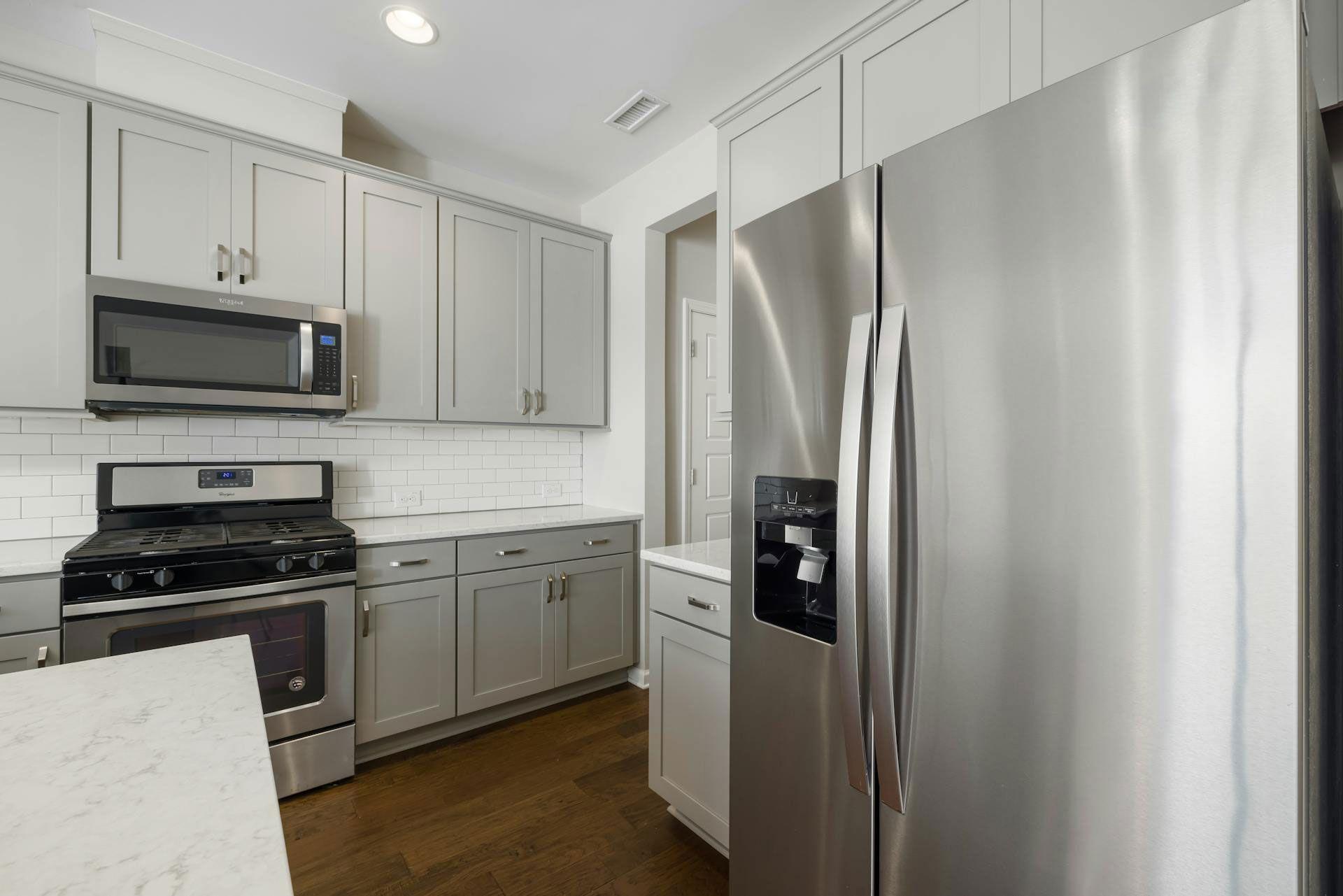 Moderne Küche mit amerikanischem Edelstahl-Kühlschrank, grauen Oberschränken, Gasherd mit Backofen.